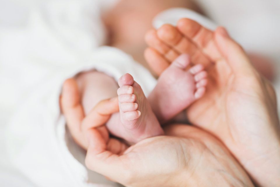 Hände umfassen vorsichtig die Füße eines neugeborenen Babys