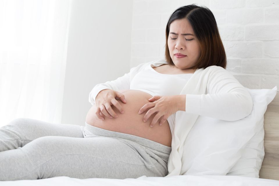 Schwangerschaftscholestase: Schwangere liegt auf dem Bett und kratzt ihren Bauch