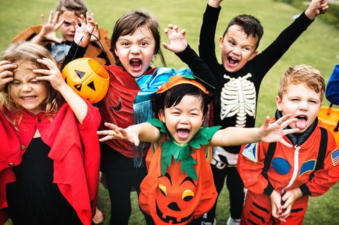Halloween-Kostüme für Kinder: Gruppe fröhlicher, verkleidete Kinder schneidet Grimassen