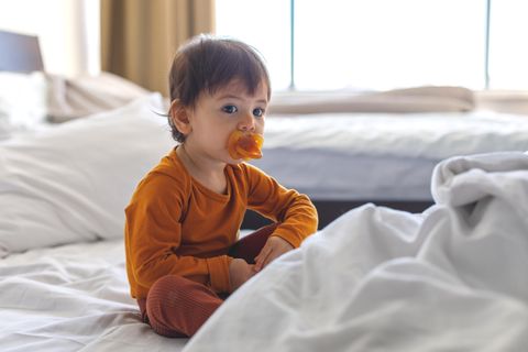 Schnullerfee: Kind sitzt mit Nuckel auf Bett