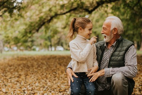 Opa sitzt mit seiner Enkelin im Herbst im Park