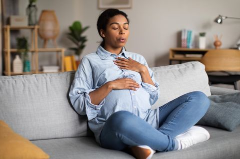 Wehen veratmen: Schwangere sitzt auf dem Sofa und atmet durch den Mund aus