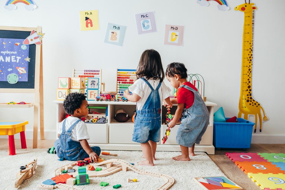 Drei Kinder spielen in einem Kinderzimmer mit verschiedenen Spielzeugen.