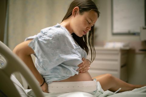 Schmerzfreie Geburt: Schwangere sitzt auf einem Bett und hält sich den Bauch
