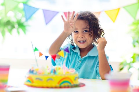 Geschenke für 4-Jährige: Kind freut sich über Geburtstagstorte und zeigt vier Finger hoch