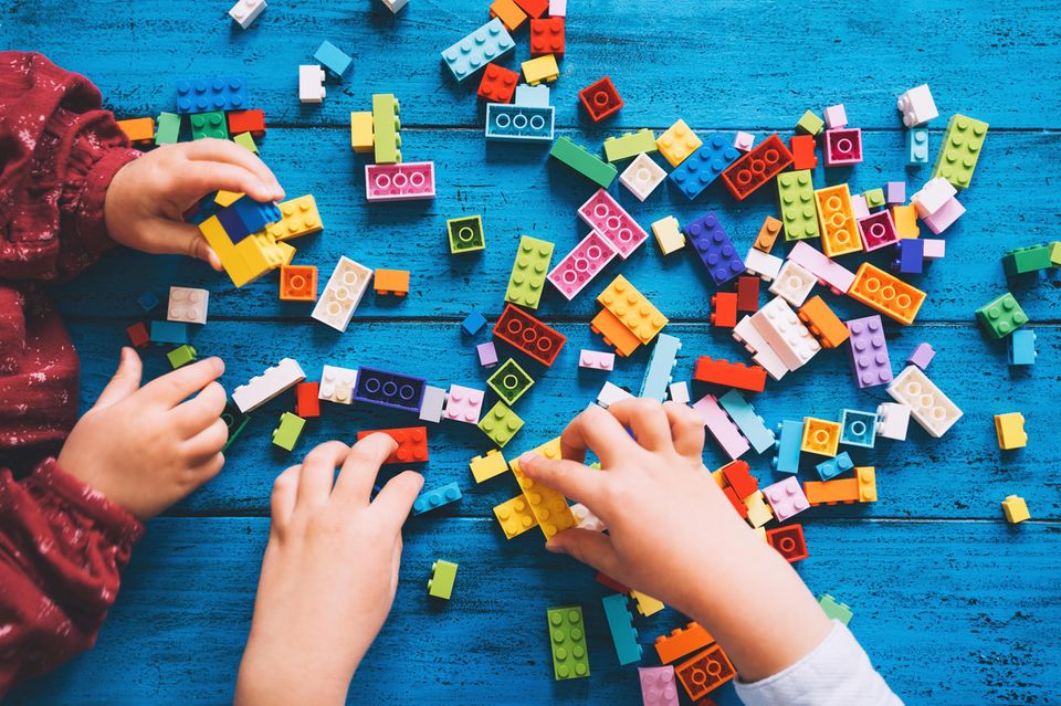 Zwei Kinder spielen mit Lego-Steinen auf einem blauen Tisch.