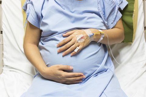 Schmerzmittel bei der Geburt: Schwangere mit Venenzugang hält sich den Bauch