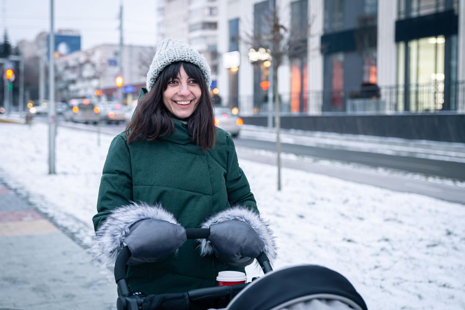 Kinderwagen-Zubehör: Frau mit Handwärmern, Kaffee und Kinderwagen im Winter