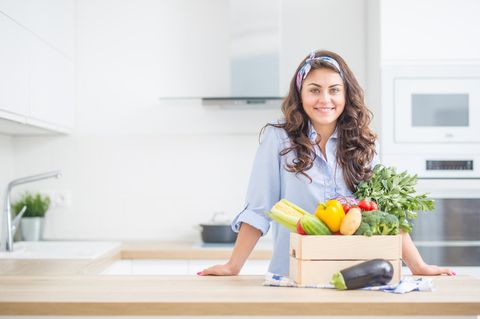 PCOS-Ernährung: Eine junge, brünette Frau steht in der Küche, vor sich eine Holzbox, gefüllt mit Gemüse