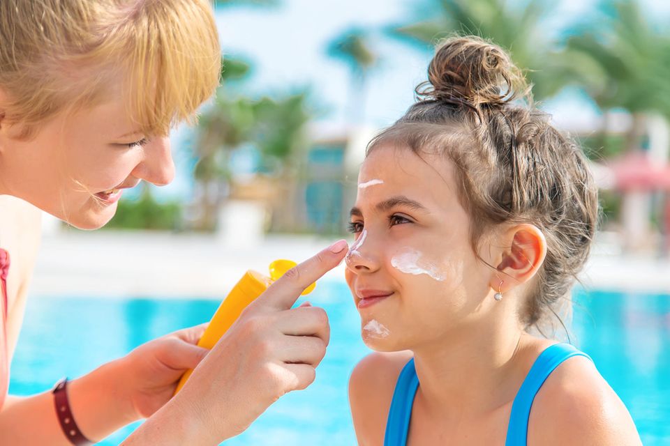 Sonnencreme für Kinder im Test: Mutter cremt Mädchen vor einem Pool im Gesicht ein.