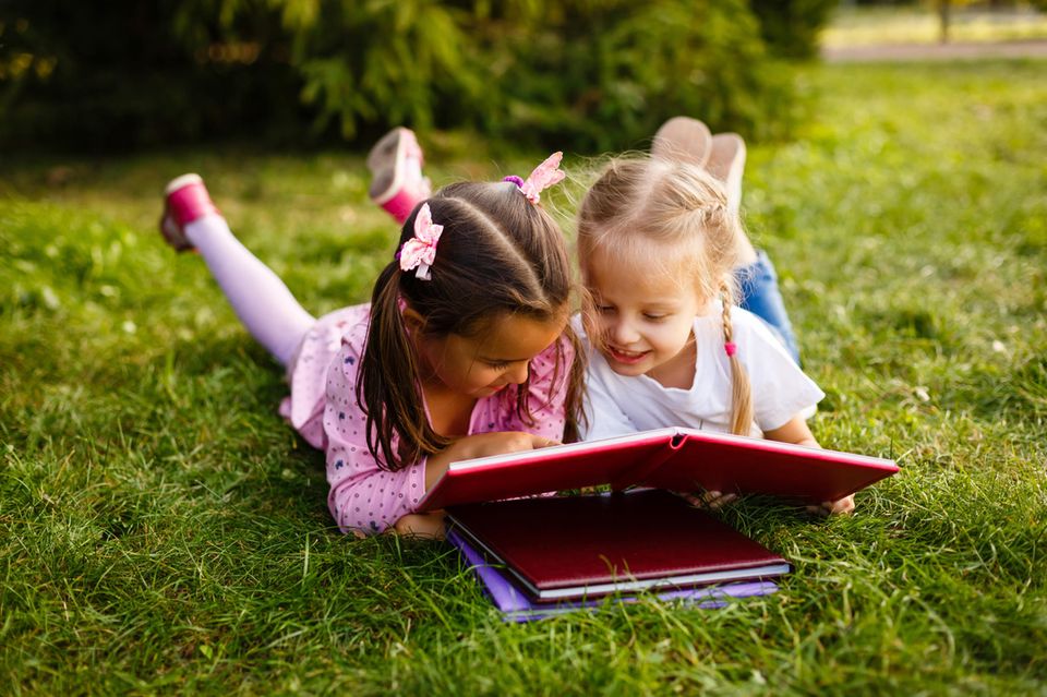 Osterbücher für Kinder: Zwei Mädchen schauen im Liegen auf der Wiese Bücher an.