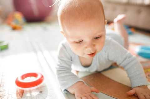 Wasserspielmatte für Babys: Ein Baby liegt in Bauchlage auf dem Boden und spielt
