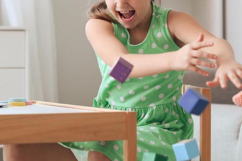 Wütendes Mädchen schleudert Spielsachen vom Tisch