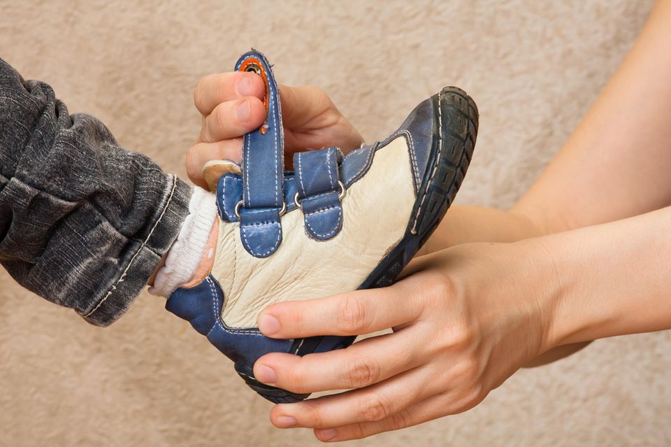 Kinderschuhe im Frühling: Hände einer Mutter, die ihrem Kind einen Schuh anzieht