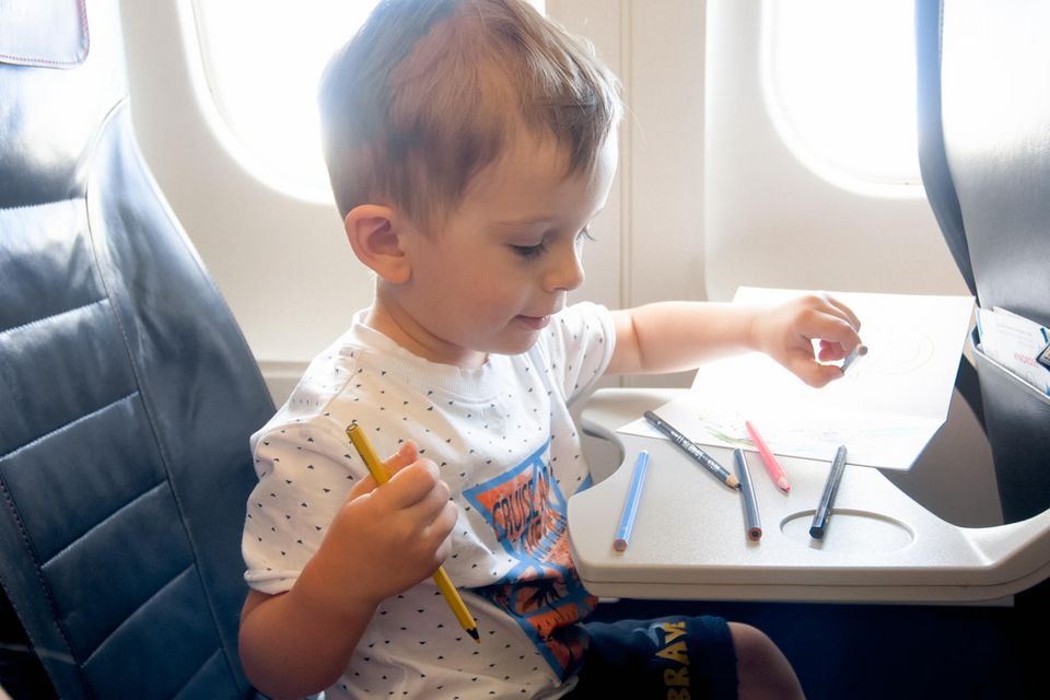 Reisegadgets: Ein kleiner Junge sitzt im Flugzeug, vor ihm liegen Buntstifte und ein Blatt Papier.