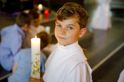 Glückwünsche zur Kommunion: Junge hält Kerze in Kirche
