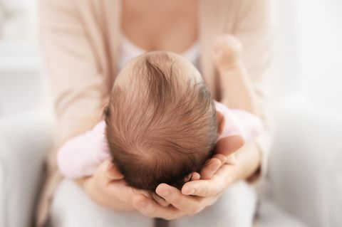 Tipps gegen einen platten Babykopf: Frau hält den Kopf eines Babys in den Händen