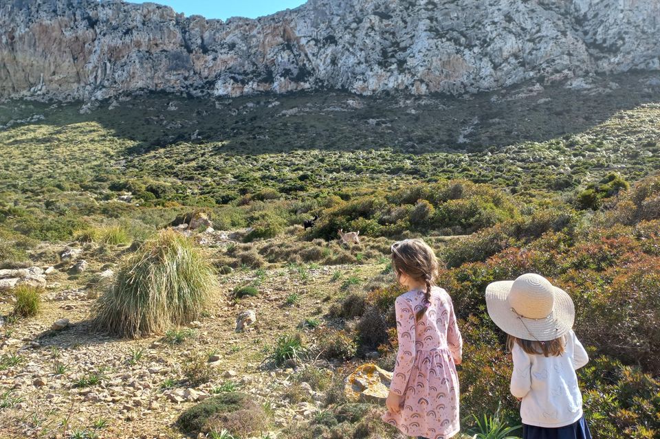 Mallorca mit Kindern: Zwei Mädchen beobachten Ziege im Gebirge.