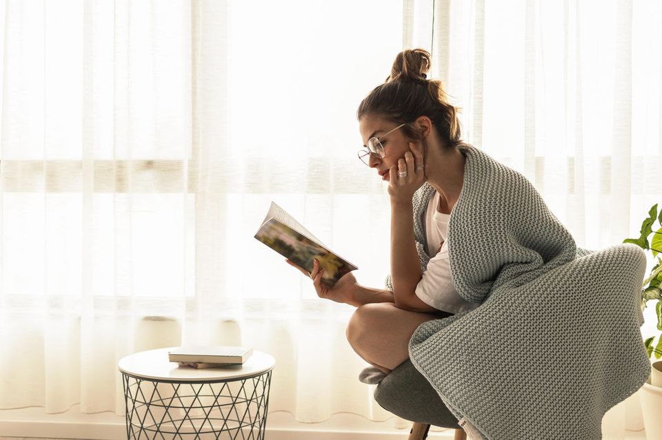 Die besten Jugendbücher: Mädchen mit Brille und Kuscheldecke liest konzentriert ein Buch.