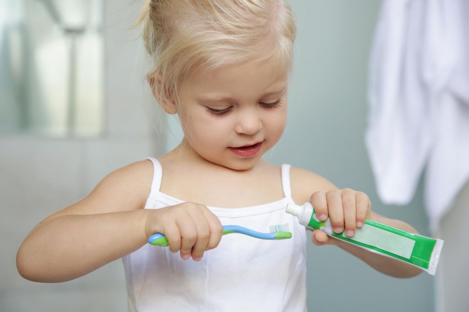 Zähne putzen Kinder: Ein kleines Mädchen macht Zahnpasta auf seine Zahnbürste