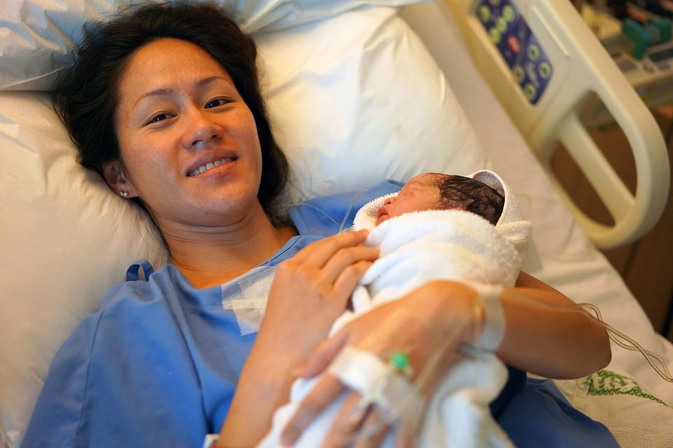 Sturzgeburt: Frau liegt mit neugeborenem Baby im Krankenhausbett