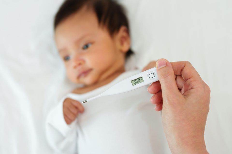 Ab wann Fieber bei Babys? Person hält ein Fieberthermometer über einem Baby