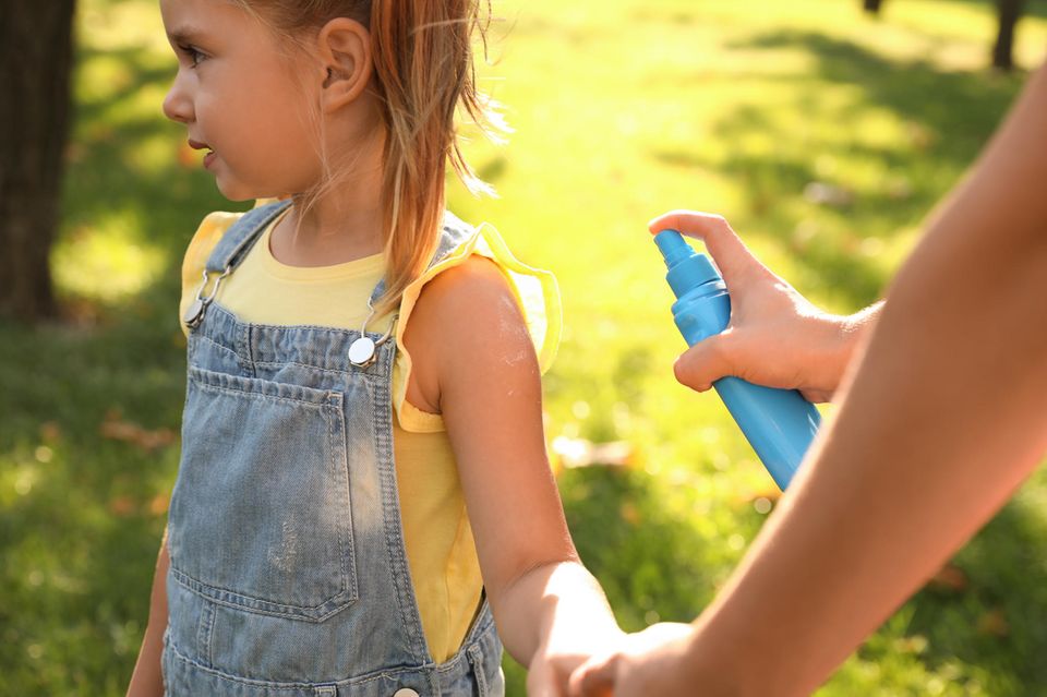 Mückenspray Test: Eine Mutter sprüht ihr Kind mit Mückenspray ein