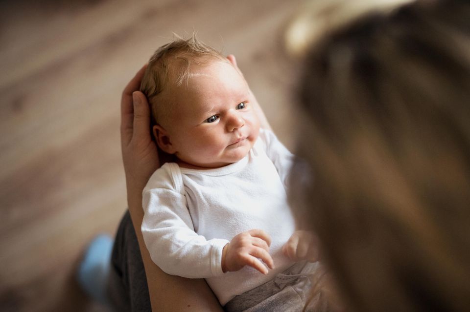 Ab wann können Babys sehen? Baby schaut eine Person an, sein Kopf in deren Händen liegend