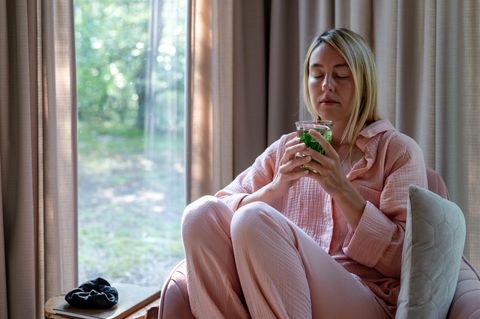 Pfefferminztee in der Stillzeit: Frau mit Becher Minztee in der Hand sitzt auf einem Sessel