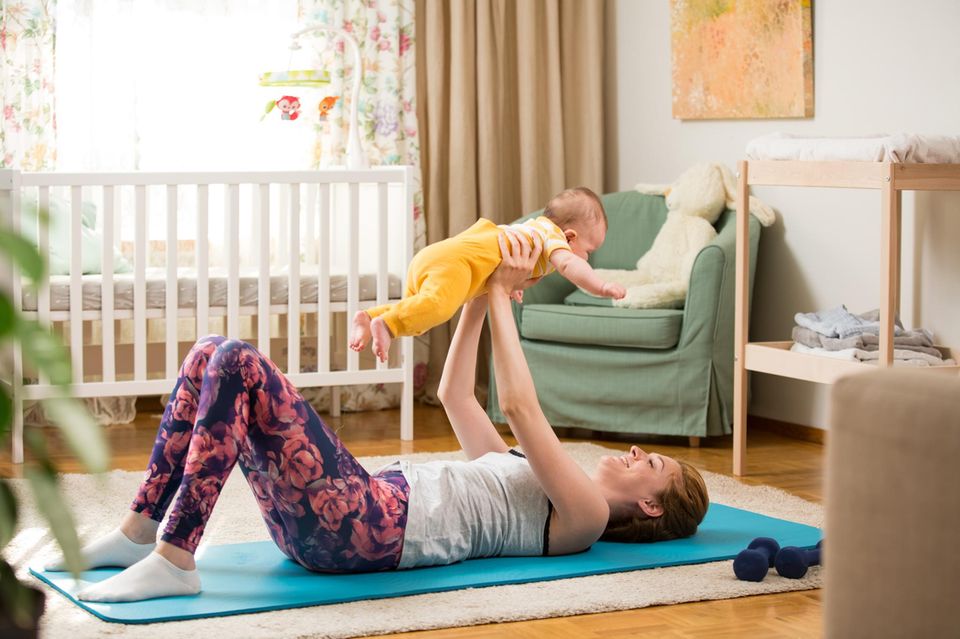 Beckenbodentraining: Frau liegt rücklings auf einer Yogamatte und stemmt ein Baby in die Luft